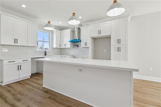 kitchen featuring white cabinetry, wall chimney range hood, and hanging light fixtures