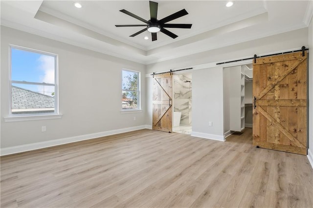 unfurnished bedroom featuring a raised ceiling, a barn door, and connected bathroom