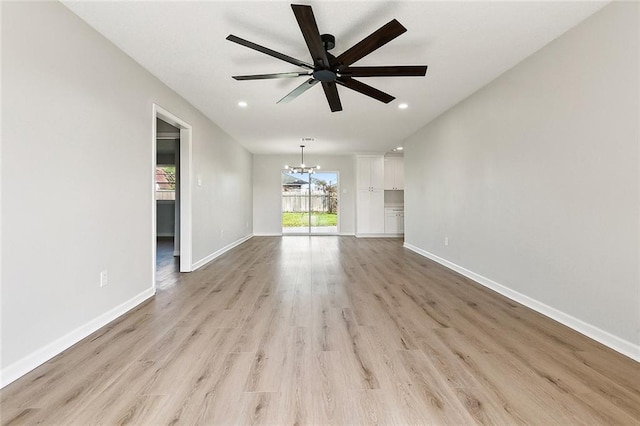 unfurnished living room featuring ceiling fan with notable chandelier and light hardwood / wood-style flooring