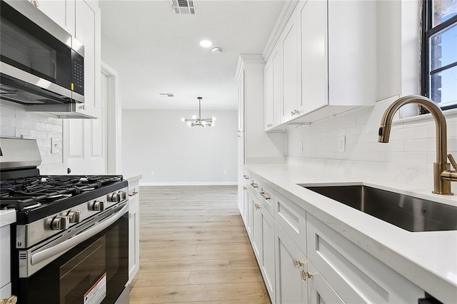 kitchen with white cabinetry, sink, hanging light fixtures, stainless steel appliances, and light hardwood / wood-style floors