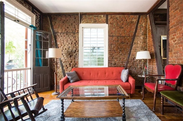 living area with crown molding, hardwood / wood-style floors, and brick wall