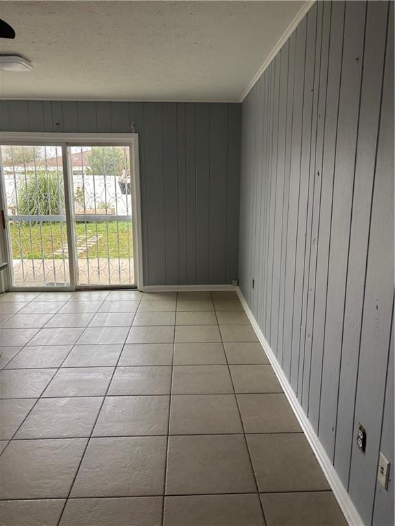 empty room featuring light tile patterned floors, baseboards, a textured ceiling, and crown molding