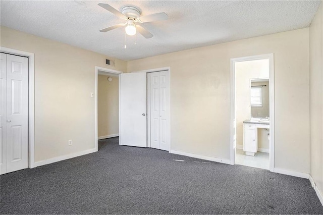 unfurnished bedroom featuring dark carpet, two closets, ensuite bath, and ceiling fan