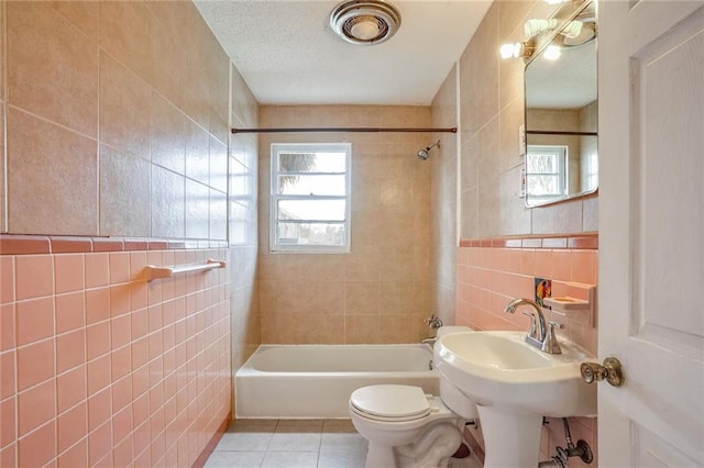 bathroom featuring tile patterned flooring, a wealth of natural light, tiled shower / bath, and tile walls