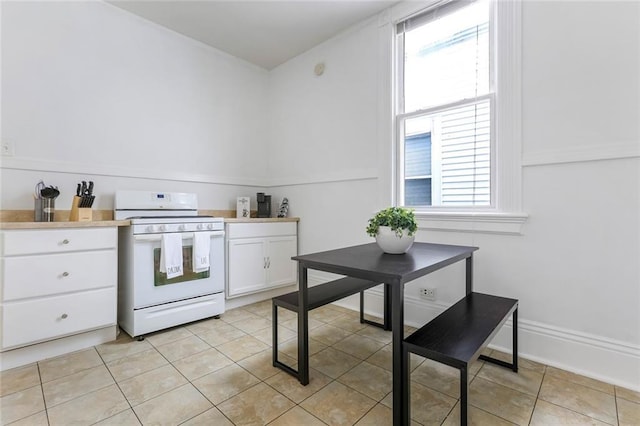 kitchen with white cabinets, white range oven, a wealth of natural light, and light tile patterned flooring