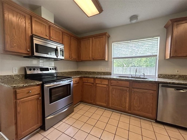 kitchen with dark stone countertops, sink, light tile patterned floors, and appliances with stainless steel finishes