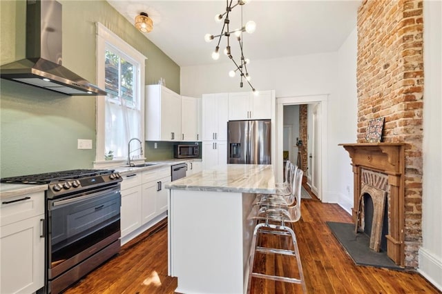 kitchen with white cabinetry, a kitchen island, wall chimney range hood, and appliances with stainless steel finishes