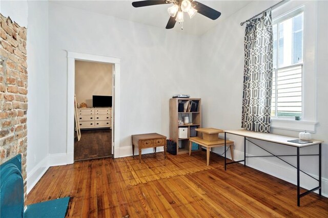 sitting room with ceiling fan, a stone fireplace, and wood-type flooring