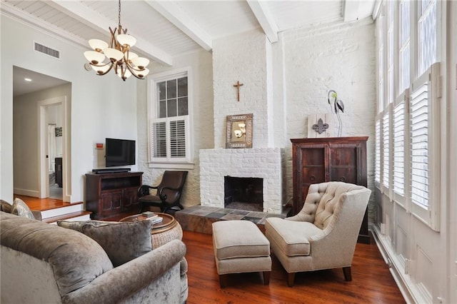 living room with beam ceiling, dark hardwood / wood-style flooring, an inviting chandelier, and a brick fireplace