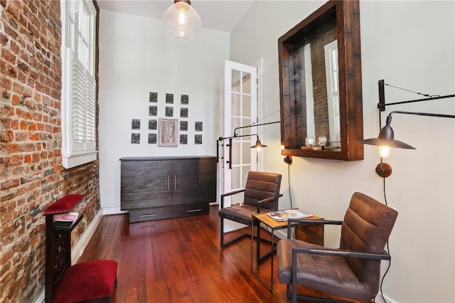 sitting room with a healthy amount of sunlight, dark wood-type flooring, and brick wall