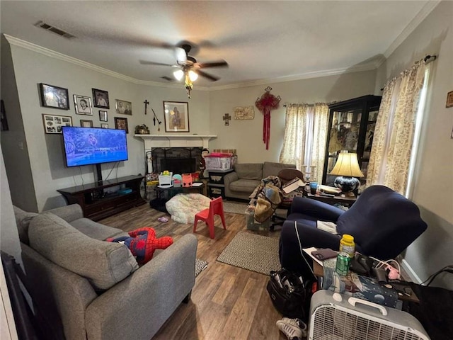 living room featuring a stone fireplace, ceiling fan, crown molding, and hardwood / wood-style flooring