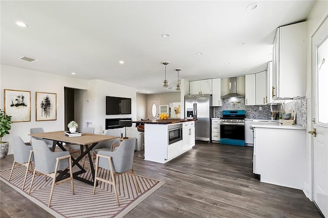 kitchen with hanging light fixtures, wall chimney exhaust hood, decorative backsplash, appliances with stainless steel finishes, and white cabinetry