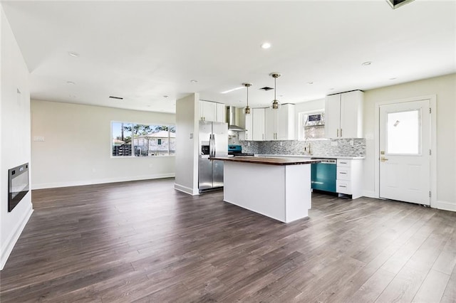 kitchen featuring appliances with stainless steel finishes, wall chimney range hood, decorative light fixtures, white cabinets, and a kitchen island