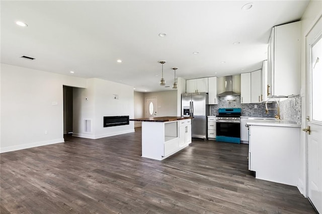 kitchen with a center island, wall chimney exhaust hood, appliances with stainless steel finishes, decorative light fixtures, and white cabinetry