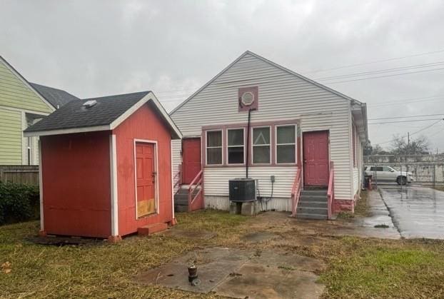 back of house featuring central air condition unit, a storage unit, and a lawn