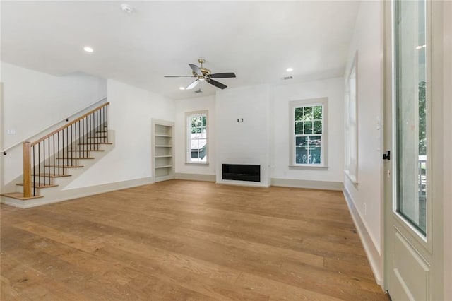 unfurnished living room featuring baseboards, recessed lighting, a fireplace, stairs, and light wood-style floors