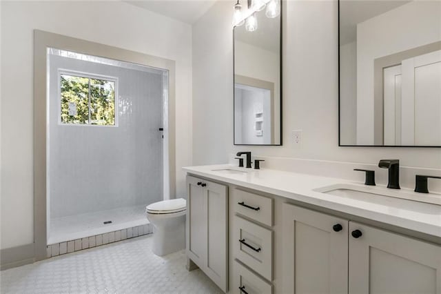 full bathroom with double vanity, toilet, a tile shower, and a sink