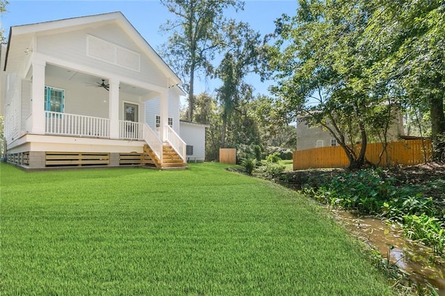 view of yard featuring covered porch, a ceiling fan, and fence