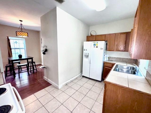 kitchen featuring stove, sink, hanging light fixtures, white fridge with ice dispenser, and light tile patterned flooring