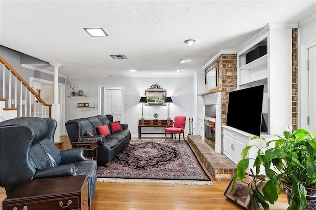 living room featuring a brick fireplace, ornamental molding, built in features, a textured ceiling, and light hardwood / wood-style floors