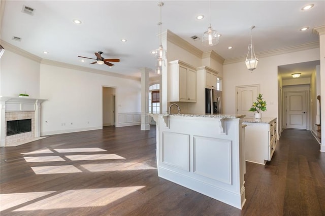 kitchen with a tile fireplace, hanging light fixtures, ceiling fan, light stone countertops, and stainless steel fridge with ice dispenser