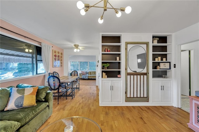 living room featuring built in features, a chandelier, and light wood-type flooring