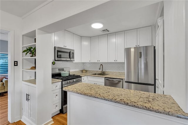 kitchen with appliances with stainless steel finishes, light stone counters, sink, light hardwood / wood-style floors, and white cabinetry