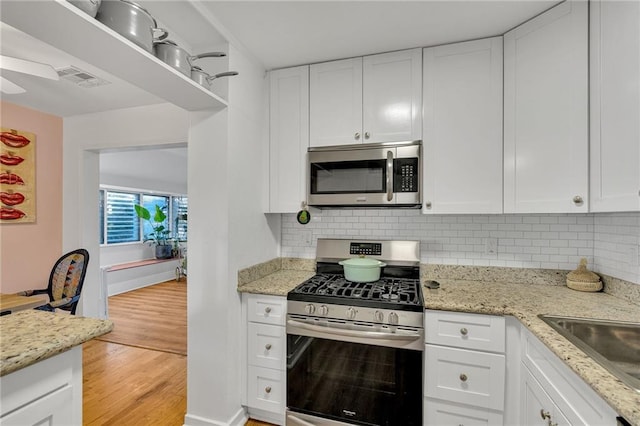 kitchen with backsplash, light hardwood / wood-style flooring, light stone countertops, appliances with stainless steel finishes, and white cabinetry