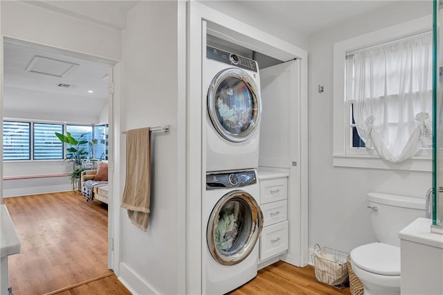 laundry room with stacked washing maching and dryer and light hardwood / wood-style flooring