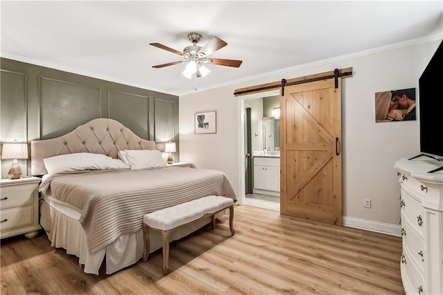 bedroom featuring ensuite bathroom, ornamental molding, ceiling fan, a barn door, and light hardwood / wood-style flooring