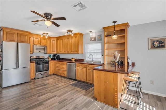 kitchen featuring kitchen peninsula, appliances with stainless steel finishes, a kitchen breakfast bar, sink, and pendant lighting