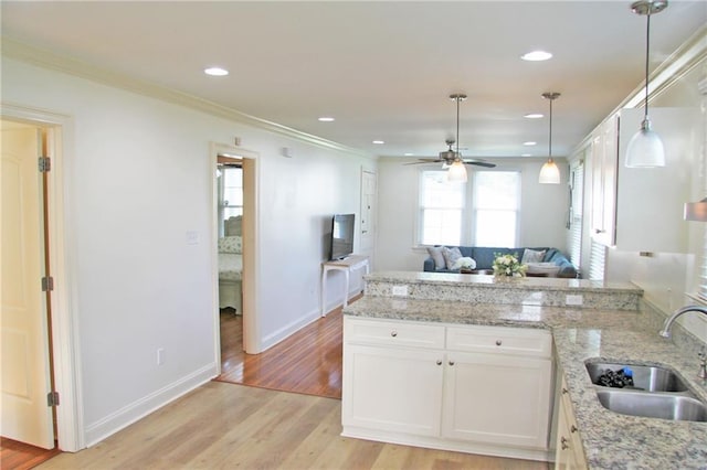 kitchen with light stone countertops, light wood-type flooring, crown molding, sink, and white cabinets