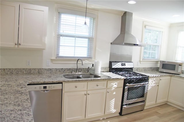 kitchen featuring light stone countertops, light wood-type flooring, wall chimney exhaust hood, stainless steel appliances, and sink