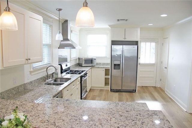 kitchen featuring sink, wall chimney exhaust hood, stainless steel appliances, pendant lighting, and white cabinets