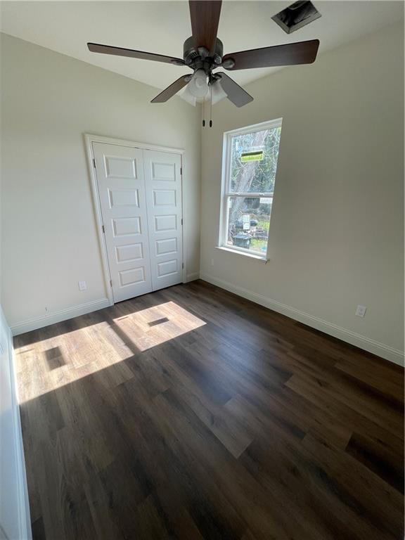 unfurnished bedroom with ceiling fan, dark wood-type flooring, and a closet