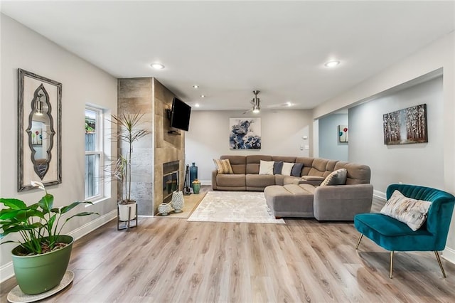 living room with a high end fireplace, light hardwood / wood-style floors, and ceiling fan