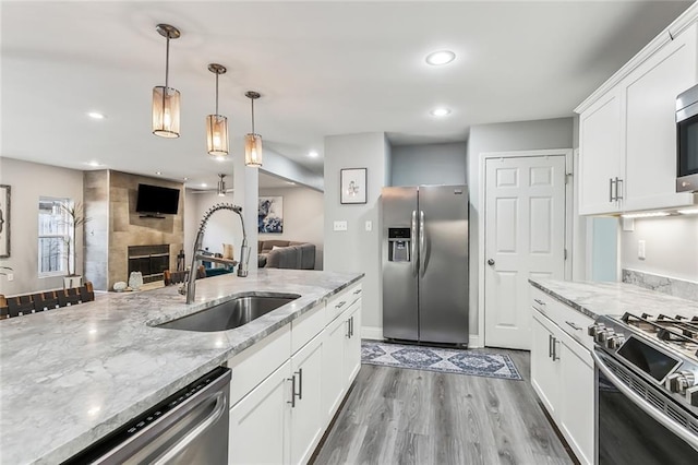 kitchen with stainless steel appliances, sink, a fireplace, white cabinetry, and hanging light fixtures