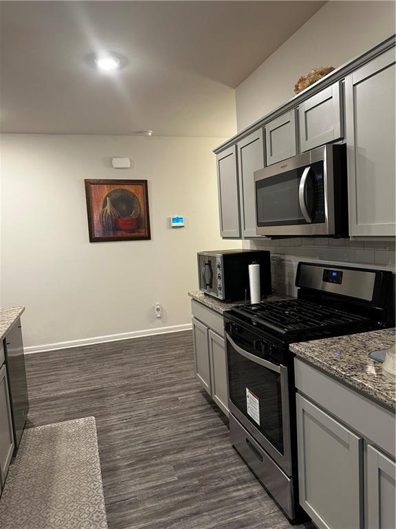 kitchen with gray cabinets, light stone countertops, and stainless steel appliances