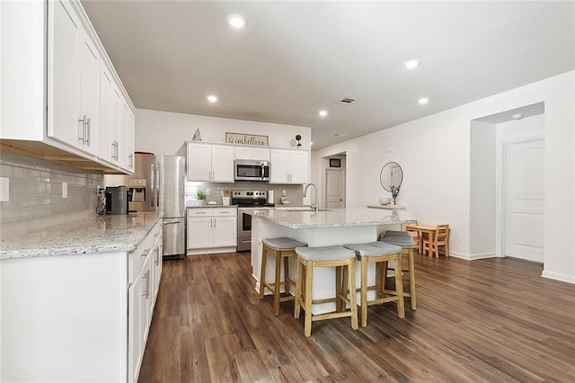 kitchen featuring sink, appliances with stainless steel finishes, white cabinets, a center island with sink, and dark wood-type flooring