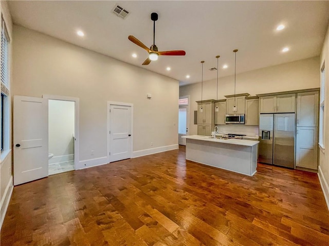 kitchen featuring stainless steel appliances, dark wood-style flooring, visible vents, light countertops, and an island with sink