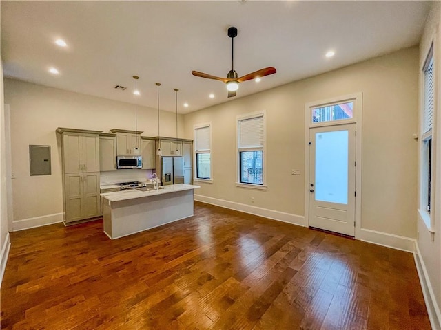 kitchen with dark wood finished floors, stainless steel appliances, light countertops, a kitchen island with sink, and electric panel