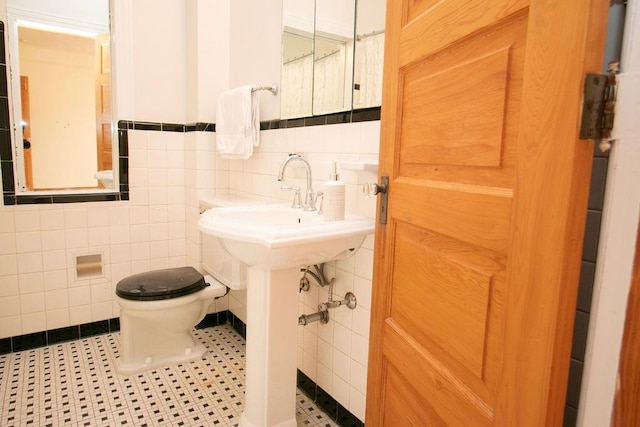 bathroom with toilet, tile patterned flooring, and tile walls