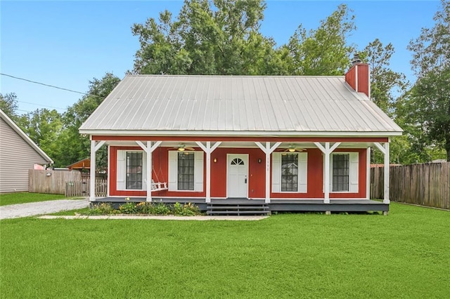 view of front of house with fence, covered porch, a chimney, a front lawn, and metal roof