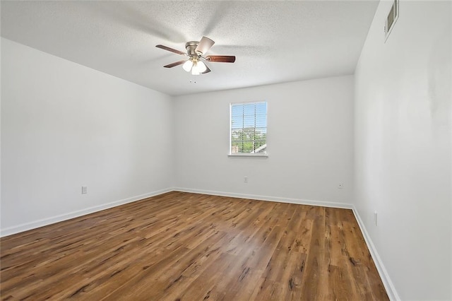 spare room featuring visible vents, baseboards, ceiling fan, wood finished floors, and a textured ceiling