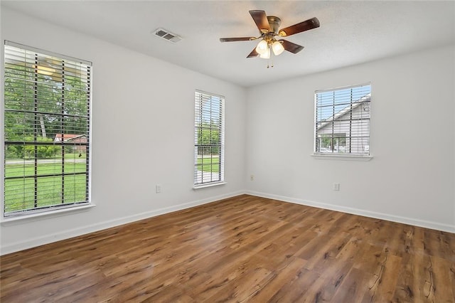 spare room featuring visible vents, plenty of natural light, baseboards, and wood finished floors