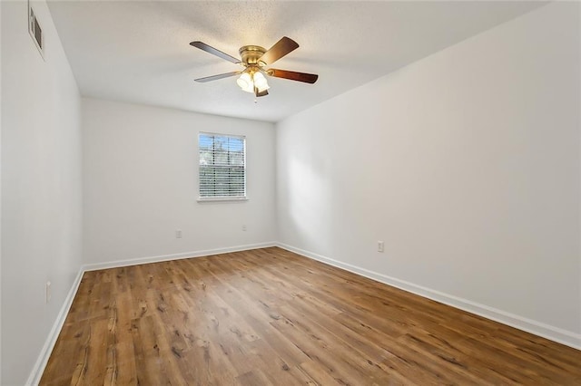 unfurnished room featuring a ceiling fan, wood finished floors, visible vents, and baseboards