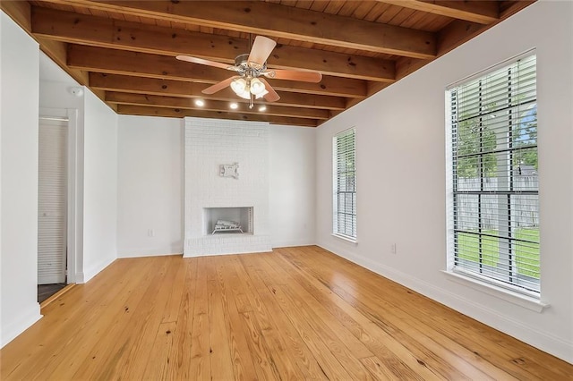 unfurnished living room featuring beam ceiling, hardwood / wood-style flooring, a fireplace, baseboards, and ceiling fan