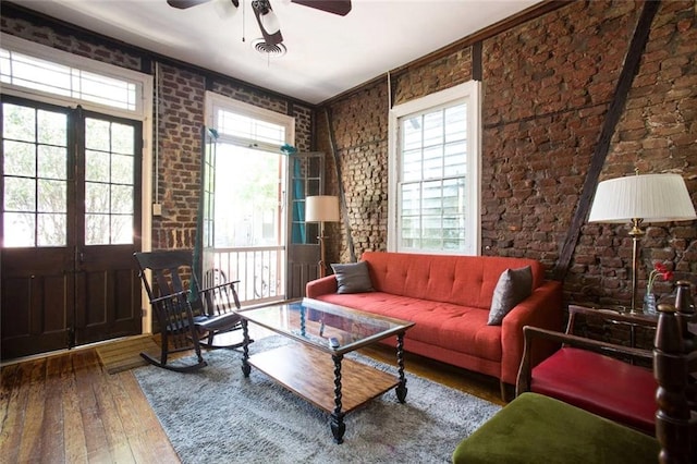 living area with hardwood / wood-style floors, ceiling fan, ornamental molding, and brick wall