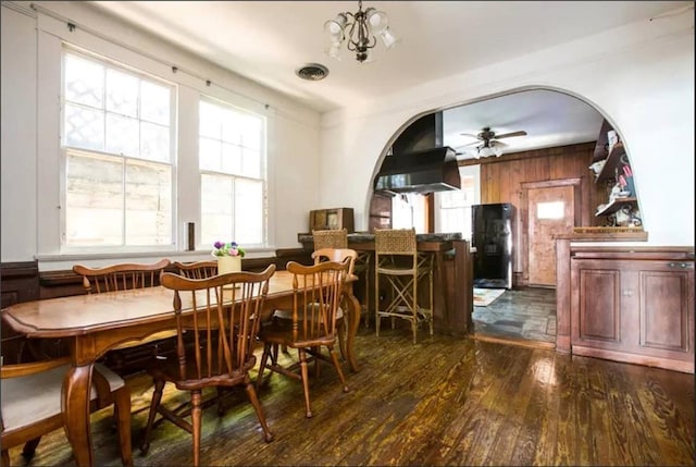 dining space featuring wood walls, dark wood-type flooring, and ceiling fan with notable chandelier