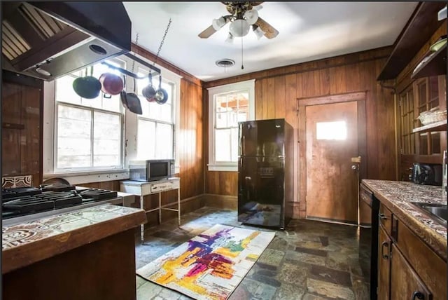 kitchen with island range hood, ceiling fan, wooden walls, and black appliances